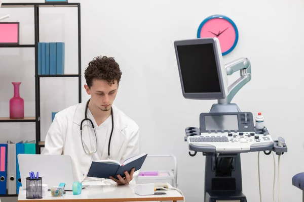 Молодой врач первичной медико-санитарной помощи рассматривает записи календаря о своих пациентах. Кабинет врача — стоковое фото