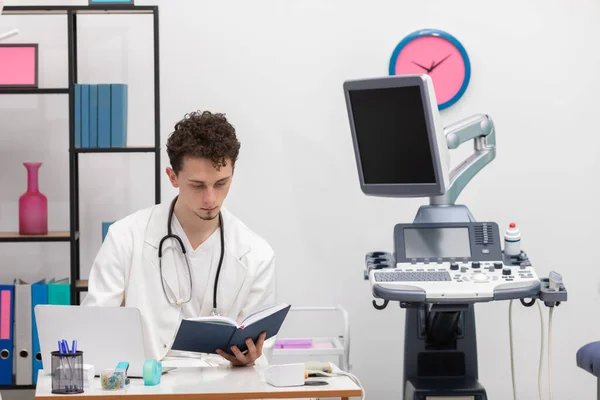 Seorang dokter perawatan primer muda meninjau entri kalender buku tentang pasiennya. Kantor dokter. — Stok Foto