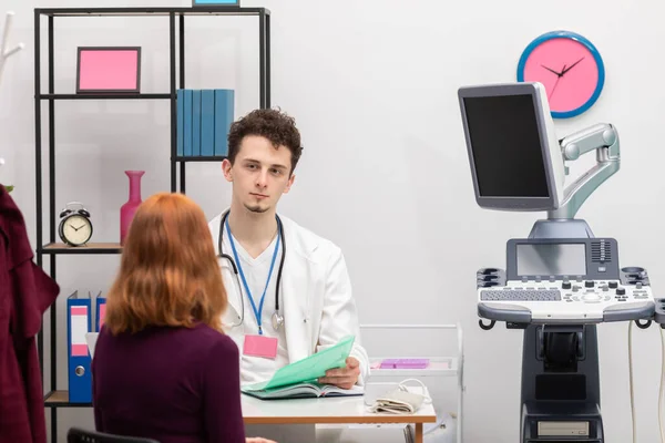 Un médico está hablando con un paciente pelirrojo con una sonrisa en la cara. Una mujer adulta en un consultorio médico. Ultrasonido gráfico —  Fotos de Stock