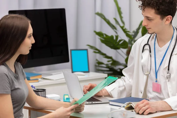 Під час розмови з пацієнтом в офісі, лікар перевіряє на ноутбуці, щоб побачити, чи готові результати тесту. Лікар первинної допомоги — стокове фото