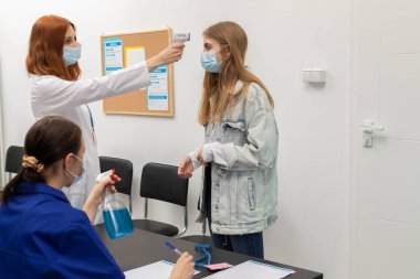 Kliniğin girişinde, bir kişi vücut ısısını ölçer ve diğeri kişisel bilgileri ve ölçülen sıcaklığı kaydeder.