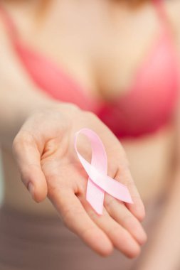 Sağ eli önünde uzanan kız, göğüs kanserine karşı verilen mücadelenin sembolü olan pembe bir kurdele tutuyor..