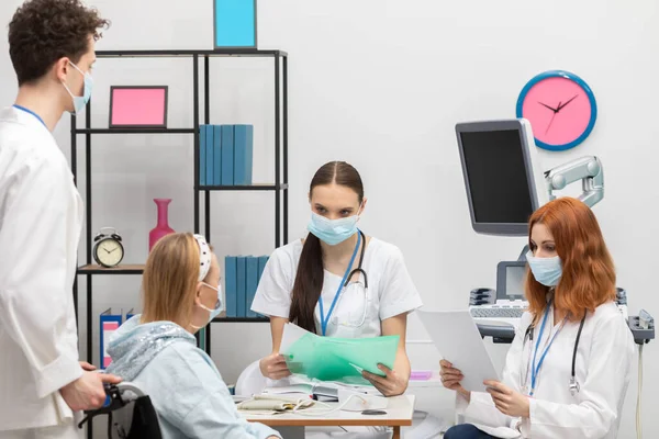 Before the visit, the doctor carefully checks the patients medical history for pandemics. A 50-year-old woman in a wheelchair in the doctors office.