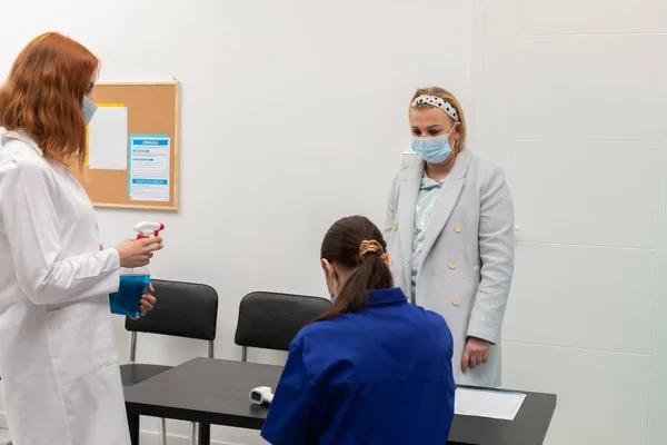 El personal médico en la entrada de la clínica registra la información personal de los pacientes y las mediciones de temperatura — Foto de Stock