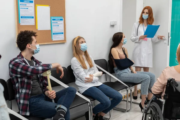 The red-haired doctor reads out the next person in line and invites you to join her in the doctors office. A protective mask over her mouth and nose.