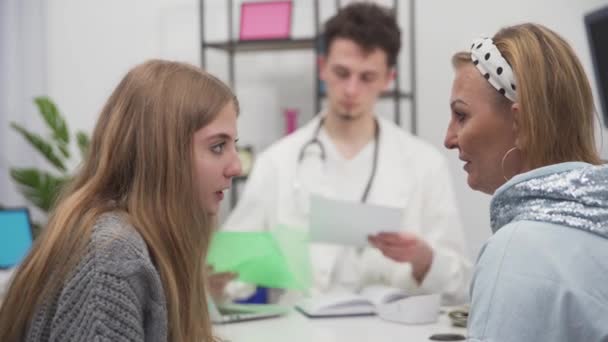 Ett lugnt och sakligt samtal mellan en mor och dotter om testresultat från en regelbunden hälsokontroll av en tonårstjej. Läkaren lämnar in dokumenten — Stockvideo