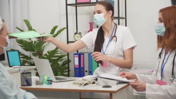 El personal médico importa a una mujer de 50 años en silla de ruedas para un chequeo periódico. Máscara de protección que cubre boca y nariz. — Vídeos de Stock