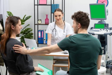 Evli bir çift bir jinekologla ofiste oturuyor. Koca hamile karısına destek oluyor. Yeşil Ekran