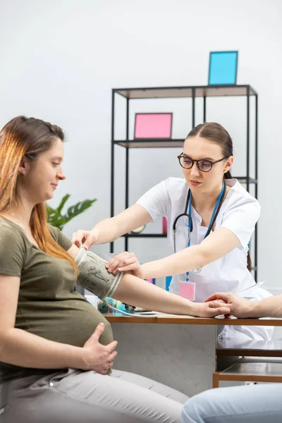 Ihr Gynäkologe legt einer Schwangeren ein Blutdruckmessgerät auf den Arm. — Stockfoto