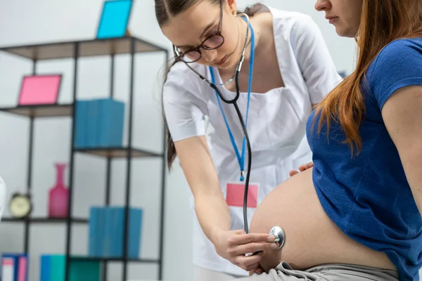 Der Arzt hört sich mit einem Stethoskop den Bauch einer schwangeren Patientin an. Berufsärztliche Praxis — Stockfoto