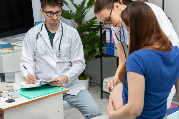 Kezelőorvosa sztetoszkóppal igazítja egy terhes beteg hasát. A kezelőorvos megfigyeli a vizsgálatot.. — Stock Fotó
