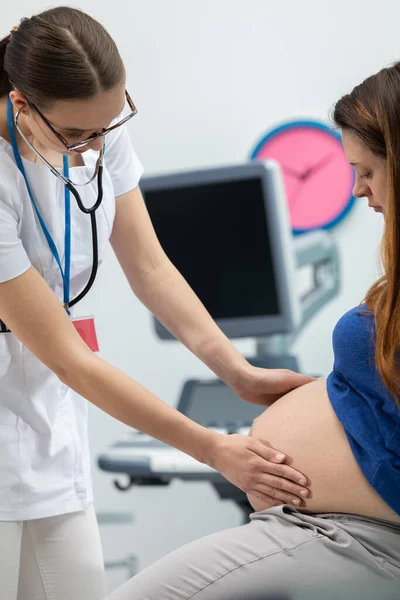 Un médico revisa el abdomen de una mujer embarazada al tocarlo con las manos. Una oficina de médicos profesionales — Foto de Stock