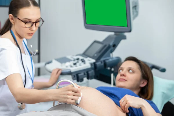 Una doctora revisa el abdomen de una paciente embarazada con un ultrasonido. Oficina de Ginecología. Pantalla verde. — Foto de Stock