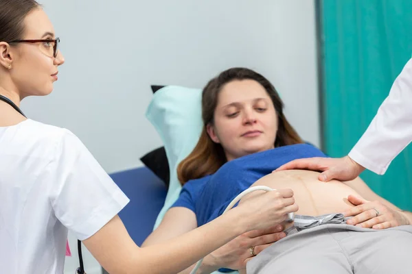Una enfermera examina el abdomen con una máquina de ultrasonido y un médico toca suavemente el abdomen de una paciente embarazada. — Foto de Stock