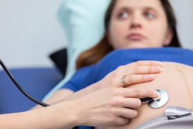 Kadın bir doktorun, hamile bir kadının karnını steteskopla taramasına yakından bakın. Profesyonel doktor ofisi.