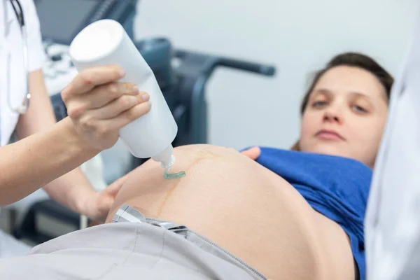 Hemşire hamile bir hastanın karnına jel sıkıyor ve ultrason için hazırlanıyor. Jinekoloji ofisi.. — Stok fotoğraf