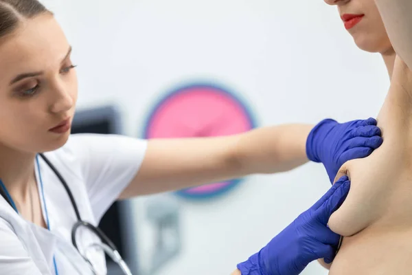 El médico lleva a cabo un examen de mama en una paciente joven, aplicando suavemente presión con las manos. Vista de primer plano. — Foto de Stock