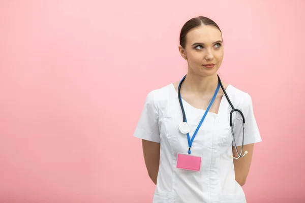 En leende kvinnlig läkare i vitt förkläde står mot en rosa bakgrund. — Stockfoto