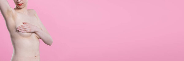 Young and naked woman with one hand raised and the other covering her breasts. Portrait on pink background. Panoramic frame.
