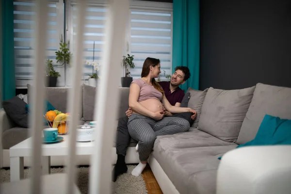 Ein Mann umarmt seine schwangere Frau. Ein Ehepaar sitzt zu Hause auf einem Sofa im Wohnzimmer. Die Schwangere. — Stockfoto
