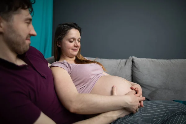 Una esposa embarazada y su marido observan como el vientre se mueve suavemente con su descendencia. Mujer embarazada.. — Foto de Stock
