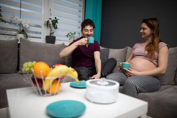 Los cónyuges se relajan en el sofá y se relajan mientras toman café. Una mujer en embarazo avanzado. — Foto de Stock