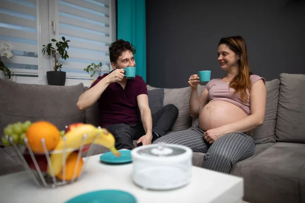 Ehepartner entspannen auf dem Sofa und entspannen beim Kaffeetrinken. Eine Frau in fortgeschrittener Schwangerschaft. — Stockfoto