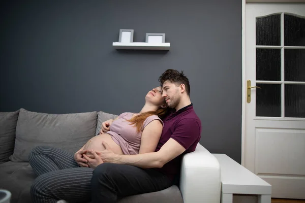 Embarazados marido y mujer sentados acurrucados en el sofá contemplando a sus hijos. Una mujer con un embarazo avanzado. — Foto de Stock