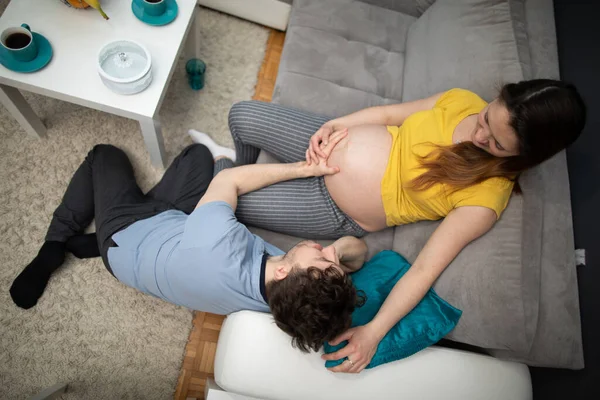 Ehemann umarmt schwangeren Frauen Bauch und sie lächeln einander an. Frau in fortgeschrittener Schwangerschaft. Blick von oben. — Stockfoto