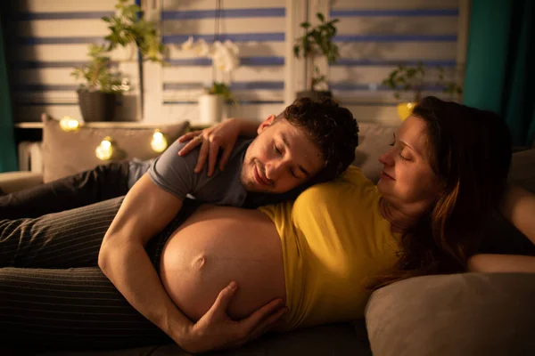 La pareja casada se acuesta en la cama y el marido abraza el vientre de las esposas embarazadas. Mujer en embarazo avanzado. — Foto de Stock