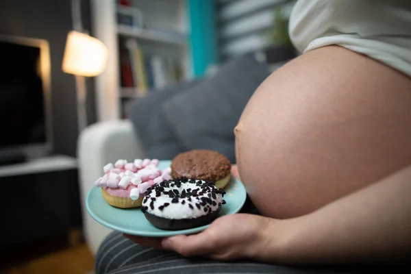 Vista lateral de una mujer de nueve meses de embarazo vientre y rosquillas dulces. Una mujer en embarazo avanzado. — Foto de Stock