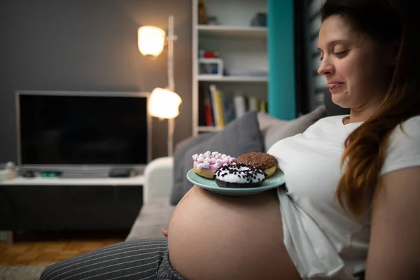 Mujer embarazada colocó donas en su vientre y lame con apetito. Una mujer en embarazo avanzado. — Foto de Stock
