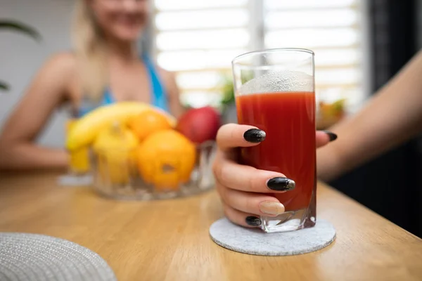 A girl is drinking a tomato jump from a glass and a friend is cheering in the background. — Stock Photo, Image