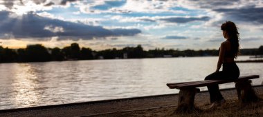 Gün batımında sakin bir bankta oturan bir kadını huzur içinde yakalayan sakin ve huzurlu bir sahne.