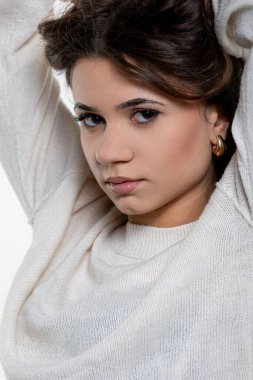 Tarz sahibi genç bir kadın şık beyaz bir kazakla şık bir moda havası yakalayarak zarif bir şekilde poz verir..