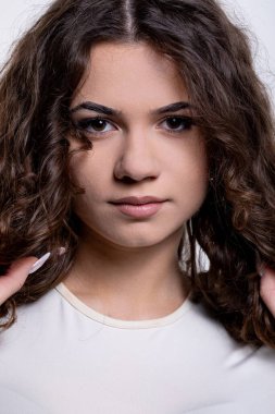 Genç bir kadının çarpıcı portresi kıvırcık saçlarını sergiliyor ve yumuşak stüdyo ışıklarında anlamlı bakışlarını gösteriyor..