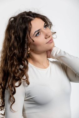 Genç bir kadın zarif bir şekilde duruyor, uzun, kıvırcık saçlarını ve derin düşüncelere dalmış ifadesini sergilerken zarafetle poz veriyor.