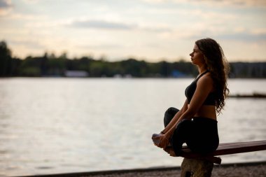 Gün batımında gölün kenarında meditasyon yapan bir kadının huzur ve huzur dolu bir sahnesi..