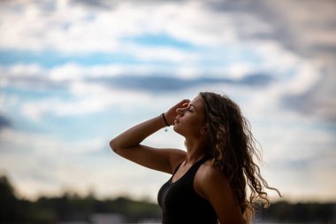 Tüylü bulutlarla dolu canlı ve dinamik bir gökyüzünün altında büyüleyici bir siluette zarif poz veren bir kadın.