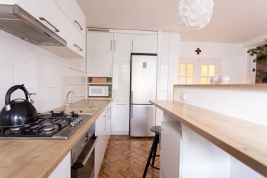 Güzel beyaz dolaplar ve konfor için sıcak ahşap bir tezgahı olan parlak ve modern bir mutfak.