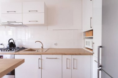 Şık ve çağdaş bir mutfak, ahşap tezgahın eşliğinde beyaz dolaplara çarpan güzel sergiler.