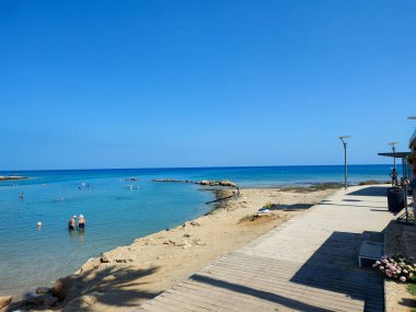 Göz kamaştırıcı güzellikte bir plaj sahnesi berrak suları sergiliyor parlak mavi gökyüzünün altında parlayan