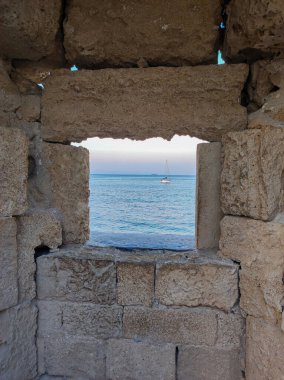 A breathtaking and captivating view of the vast sea elegantly framed by the window of an ancient stone structure