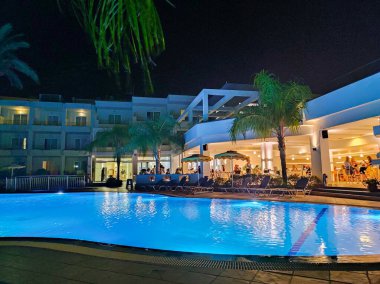 Parlak bir havuzu ve canlı bir ambiyansı olan lüks bir otelin sergilendiği güzel sakin bir gece manzarası.