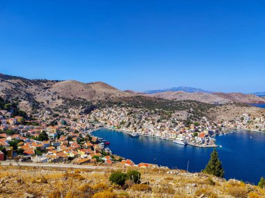 A breathtaking landscape showcases a picturesque harbor framed by colorful homes and rolling, lush hills