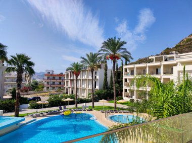 Havuzu, palmiyeleri ve açık mavi gökyüzü altında modern mimarisi olan güzel bir tatil köyü..