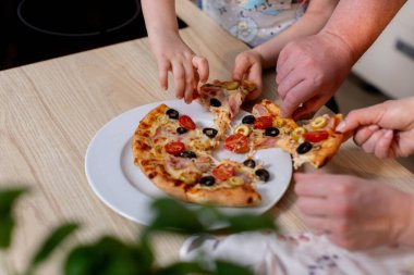 Neşeli toplanma, taze yapılmış peynirli pizza dilimlerinin etrafında toplanıyor. Aile ve arkadaşlar sıcak pizza eşliğinde çeşitli sebzeler ve erimiş peynirle kaynaşıyor.