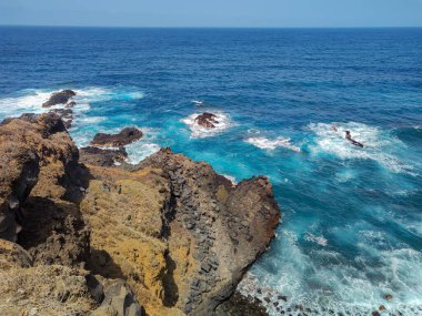 Okyanusun canlı mavi dalgalarının yanında dramatik kayalık uçurumları gösteren nefes kesici bir deniz manzarası.