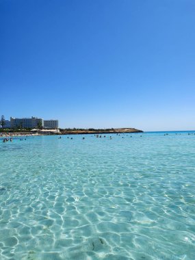 Güzel ve pitoresk bir plaj sahnesi berrak, turkuaz suları yukarıda canlı mavi bir gökyüzünün altında sergiliyor