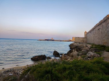 Alacakaranlıkta canlı bir denizin yanında taş bir duvarı olan çarpıcı bir kıyı manzarası güzellikleri gözler önüne seriyor.